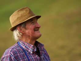 Senior farmer in a hat gazing happily outdoors, embodying joy and simplicity.
