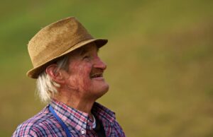 “El cambio de Don Pedro: Buenas Prácticas Agrícolas que transforman vidas” Senior farmer in a hat gazing happily outdoors, embodying joy and simplicity.