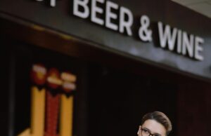 Cerveza o vino: ¿Qué bebida es más saludable según la ciencia? Stylish man in glasses and suit posing outdoors near café in a city environment.