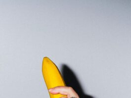 A vibrant yellow banana held in a hand with a decorative ring, staged against a neutral background.