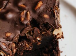 Close-up of a decadent chocolate brownie with nuts on a white plate.