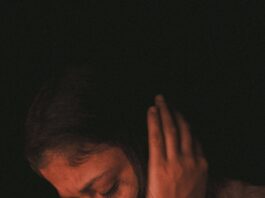 A woman in deep thought, covering ears in a dimly-lit mood, highlighting introspection.