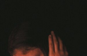 Lo que no sabías sobre la depresión: una historia que toca a todos A woman in deep thought, covering ears in a dimly-lit mood, highlighting introspection.